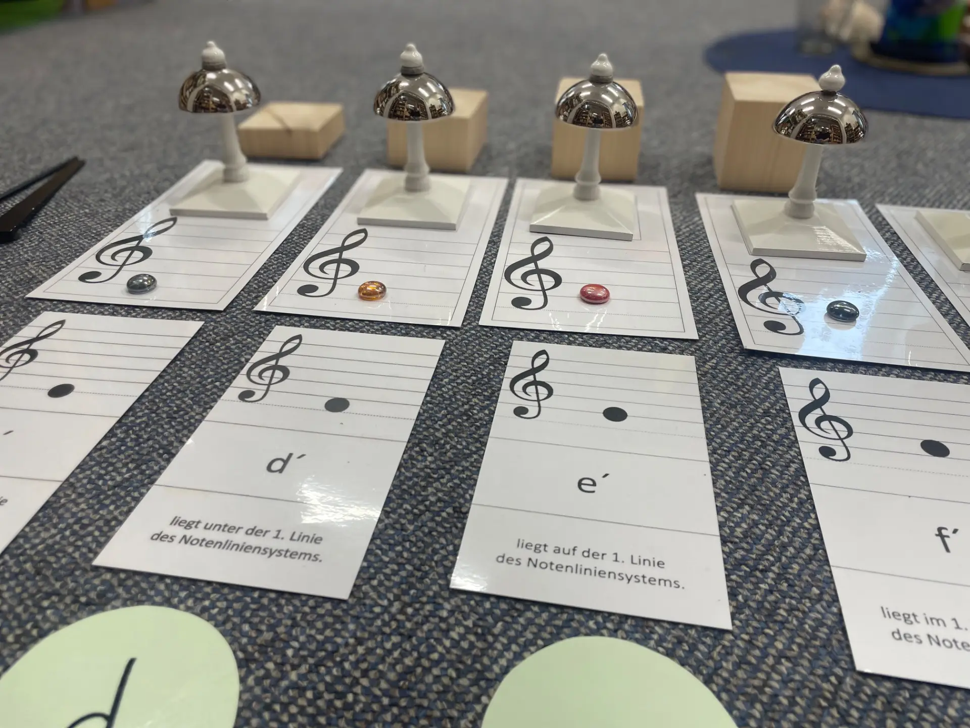 Karten mit Notensymbolen liegen auf dem Boden, daneben die passenden Montessori-Glocken.