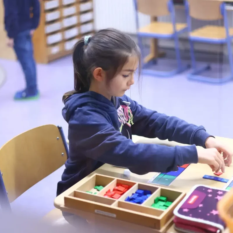 Schülerin sortiert Perlenmaterial und arbeitet an einem Montessori-Mathematikprojekt.