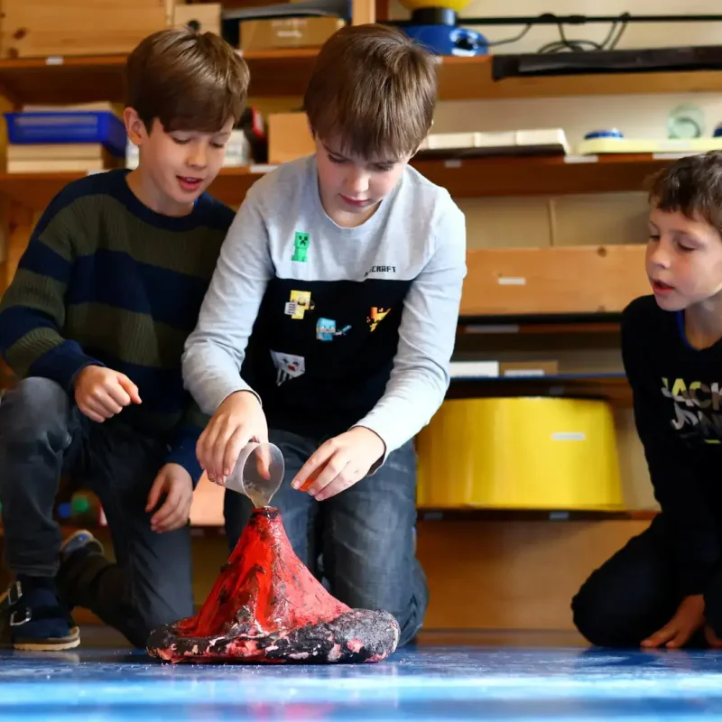 Kinder betrachten einen brodelnden Vulkanversuch und arbeiten gemeinsam am Projekt.