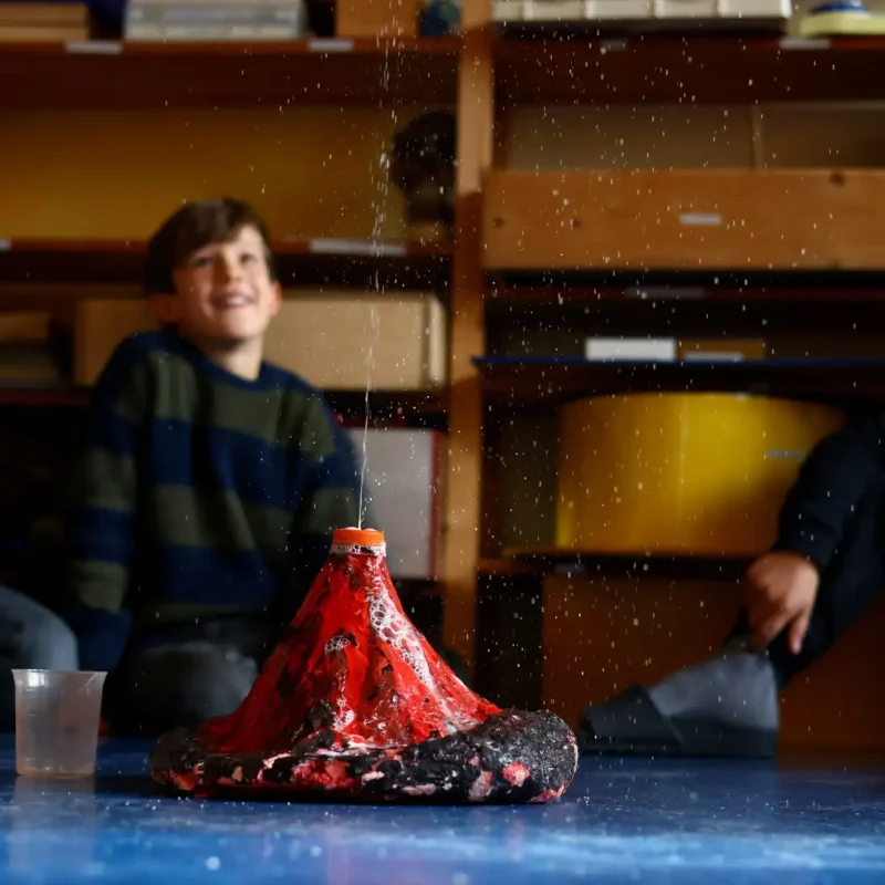 Kinder experimentieren mit einem selbstgebauten Vulkanmodell im Unterricht.