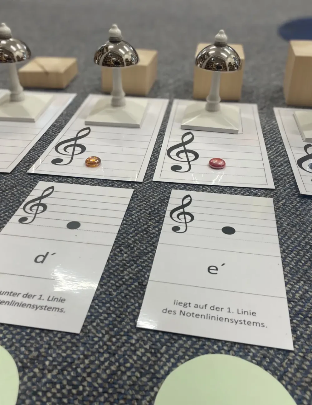 Karten mit Notensymbolen liegen auf dem Boden, daneben die passenden Montessori-Glocken.