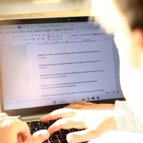 Laptop mit Textdokument, Kind tippt an einer Schreibaufgabe.