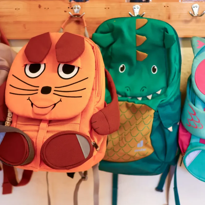 Kinderrucksäcke in Tieroptik hängen nebeneinander an Haken im Kindergartenbereich.