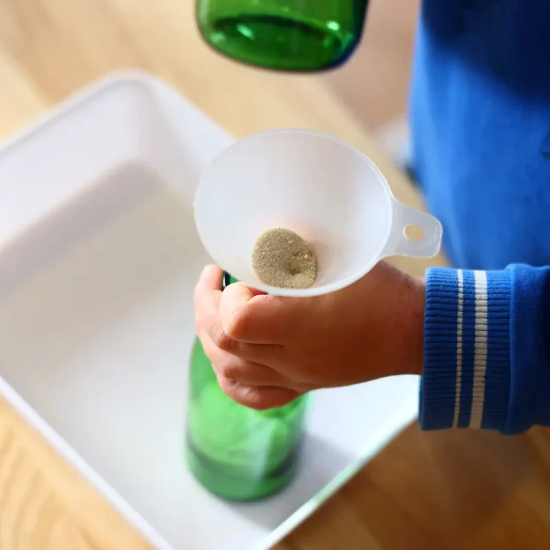 Kind führt ein Experiment mit einem Trichter und einer Karaffe durch, Lernen durch praktische Erfahrung.