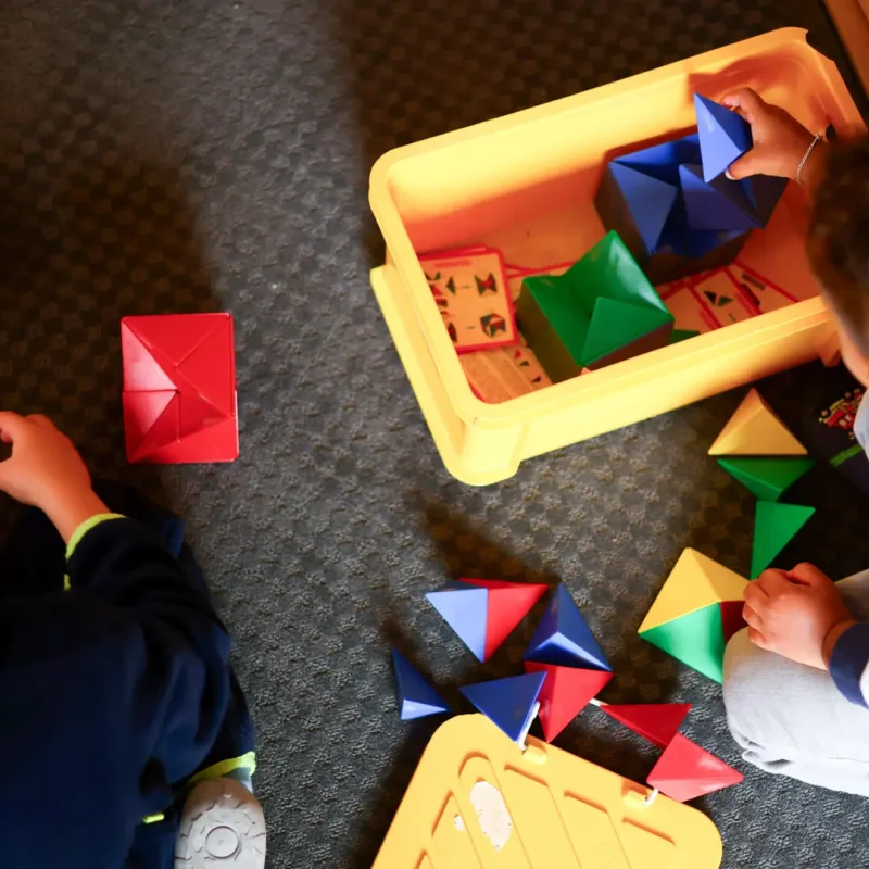 Kind spielt mit bunten geometrischen Montessori-Bausteinen und sortiert sie in einer Kiste.