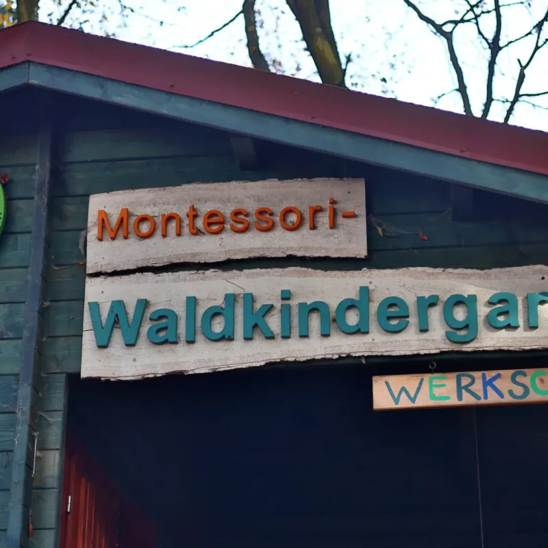 Holzschild des Montessori-Waldkindergartens an der Außenwand eines kleinen Gebäudes.