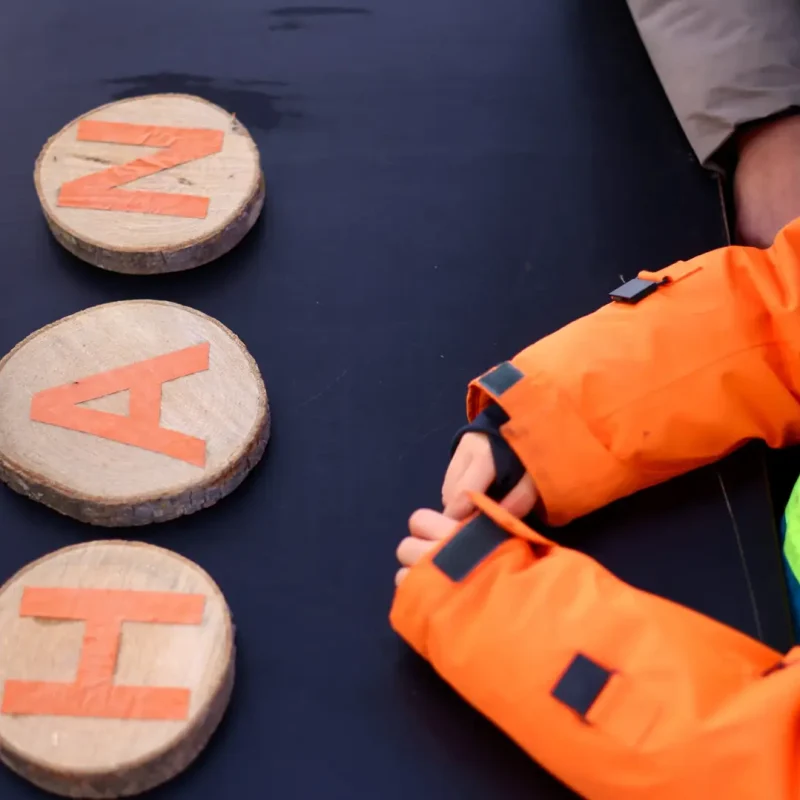 Kinderhände sortieren Holzbuchstaben auf Waldscheiben und formen einfache Wörter.