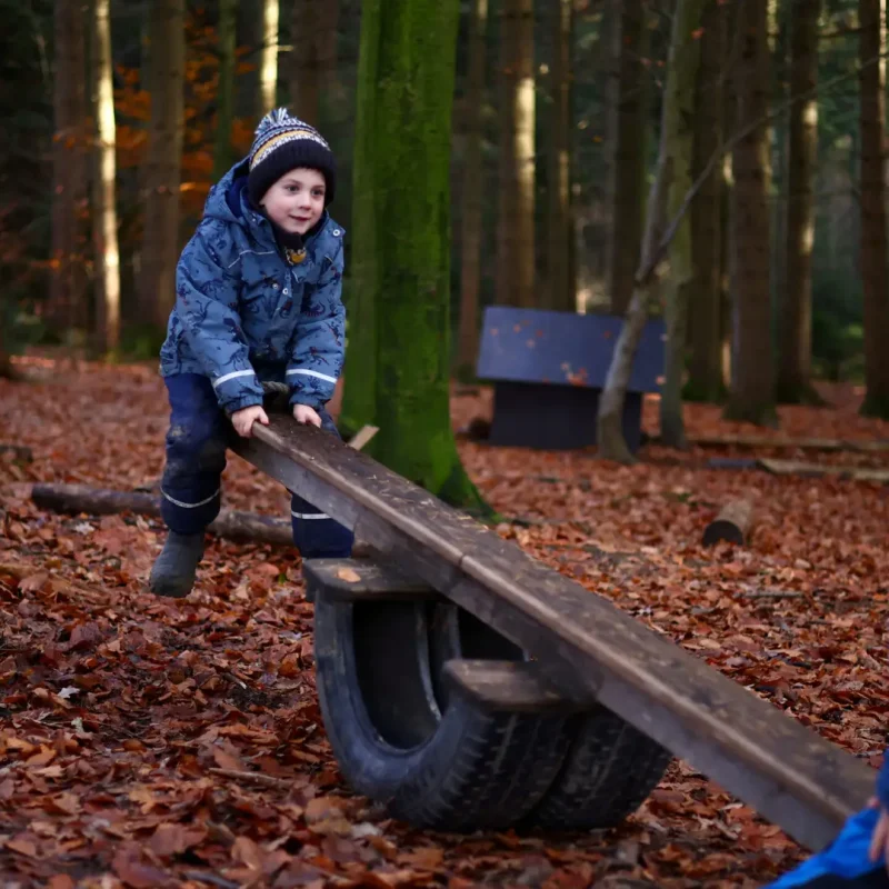 Kind balanciert auf einer Wippe aus Holz und übt Koordination im Freispiel.