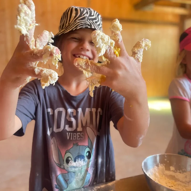 Junge knetet Teig und lächelt stolz in die Kamera während einer praktischen Lernaktivität.